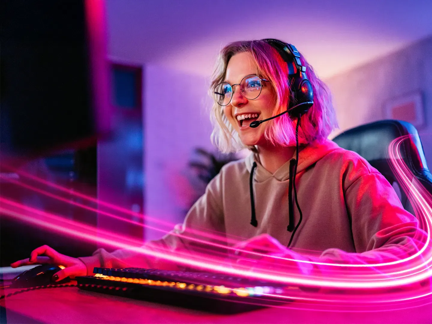 A young woman wearing a headset and glasses smiles while gaming at a computer, surrounded by glowing pink and purple neon light trails.